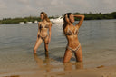 half naked swim low tide 2026 bikinis - Two women modeling leopard-print bikini sets standing in shallow water on a beach, with boats and trees in the background.